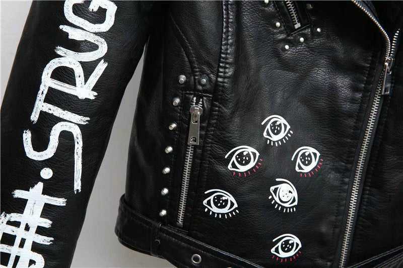 Close-up of women's faux leather motorcycle jacket featuring unique eye prints and studded details.