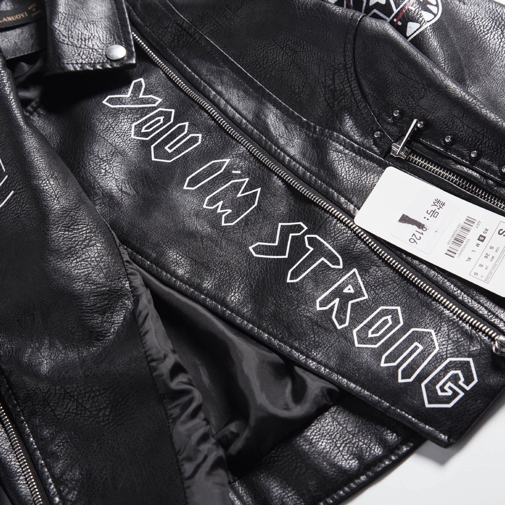 Close-up of a black faux leather motorcycle jacket with 'YOU I'M STRONG' embroidery and zippers, showcasing its edgy rock style.