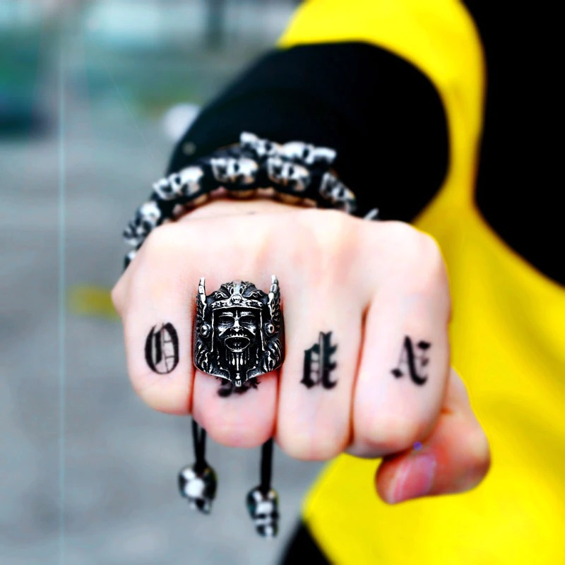 Scandinavian stainless steel ring with Odin's head design worn on a hand with tattoos and a bracelet.