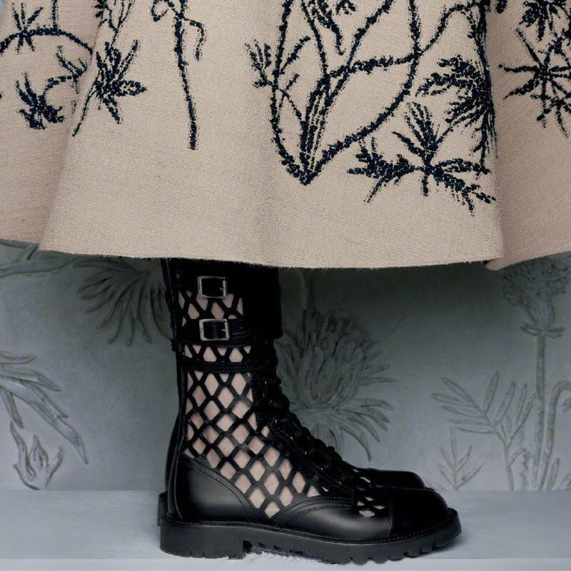Close-up of stylish black lace-up boots with metal buckles, paired with a cream embroidered skirt.