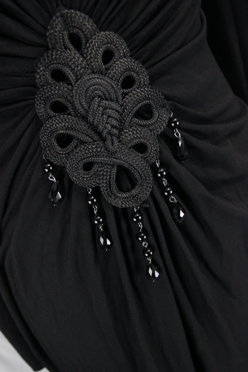 Close-up of elegant black dress detail featuring a decorative knot design with hanging beads.