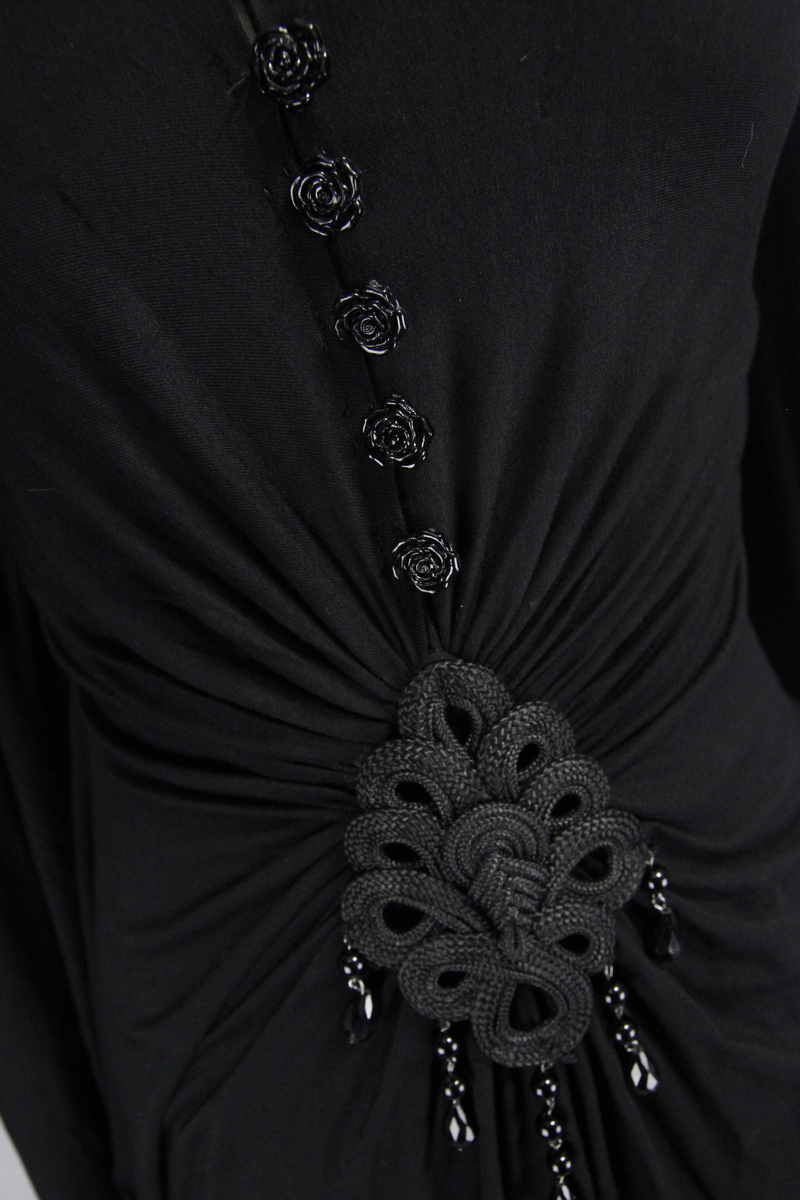 Close-up of elegant black dress with intricate floral buttons and unique decorative insert, showcasing gothic style.