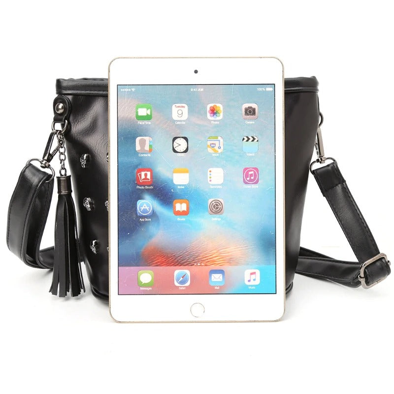 Stylish black rock-style shoulder bag with skulls, featuring an iPad for scale and stylish tassel detail.