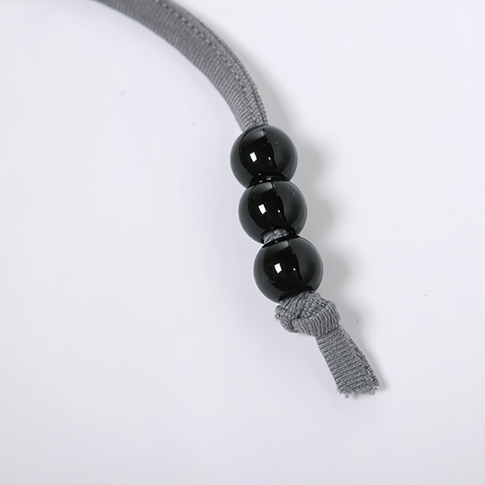 Close-up of a grey cord with three shiny black beads and a knotted end, showcasing stylish design and craftsmanship.