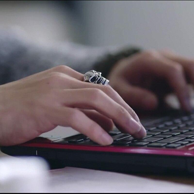 Close-up of a hand wearing a pirate skeleton ring while typing on a laptop keyboard.