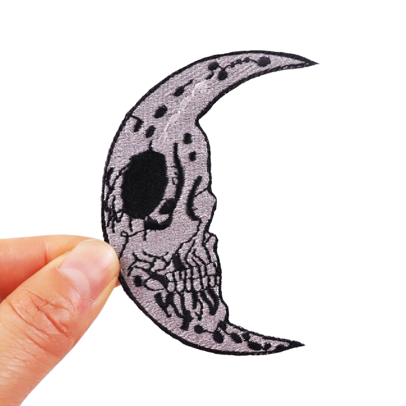 Hand holding a skull moon patch, a gothic accessory for decorating clothing in a unisex rock style.