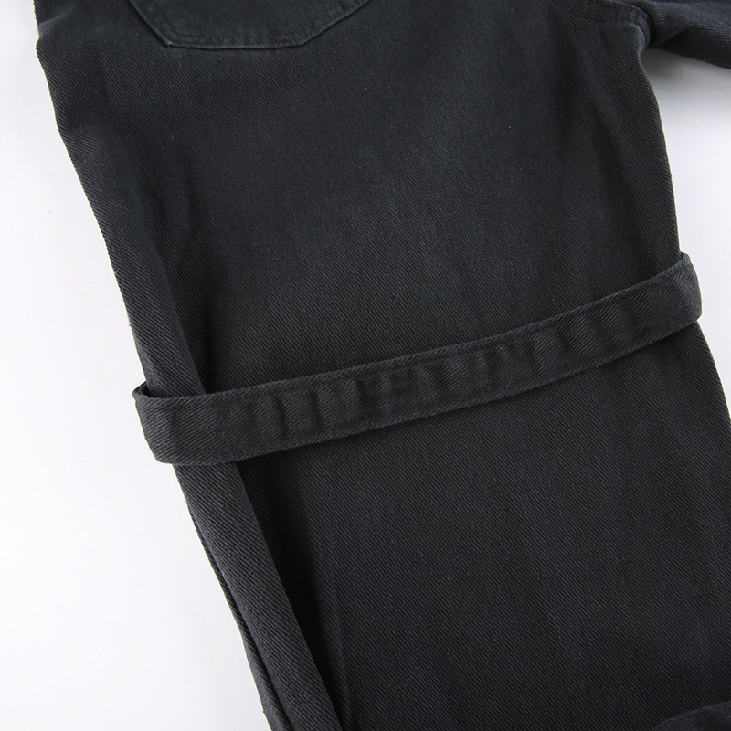 Close-up of black gothic style women's buckle pants with belt detail and textured fabric.