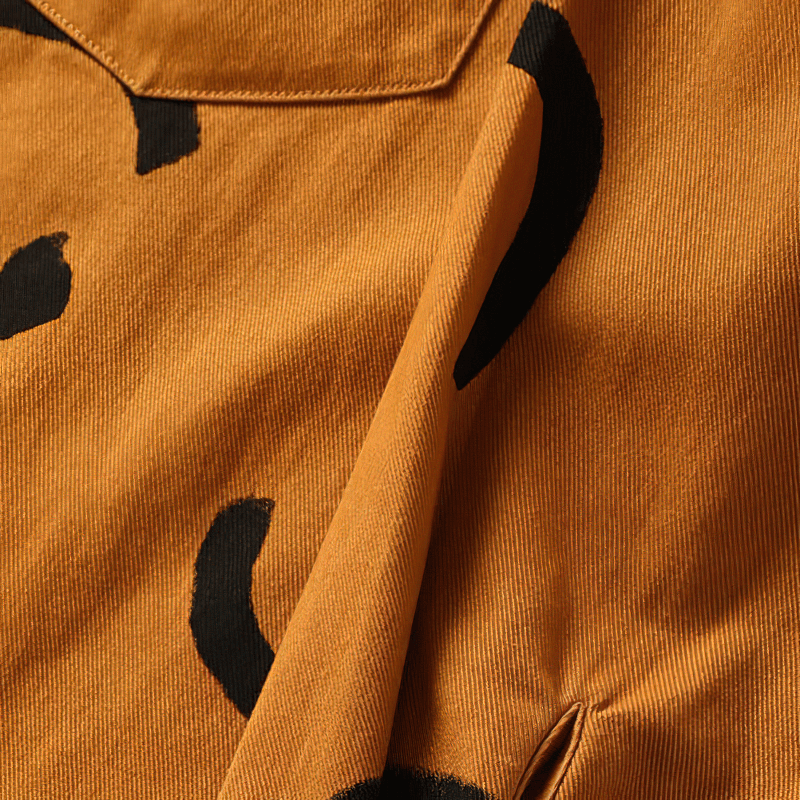 Close-up of a trendy orange cotton fabric featuring playful black smiley print design, perfect for casual men's shirts.