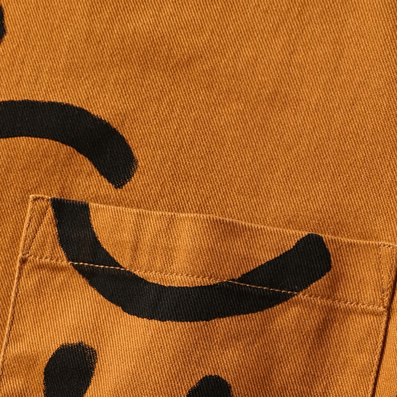 Close-up of a men's cotton shirt pocket featuring a cheerful smiley print on warm orange fabric.