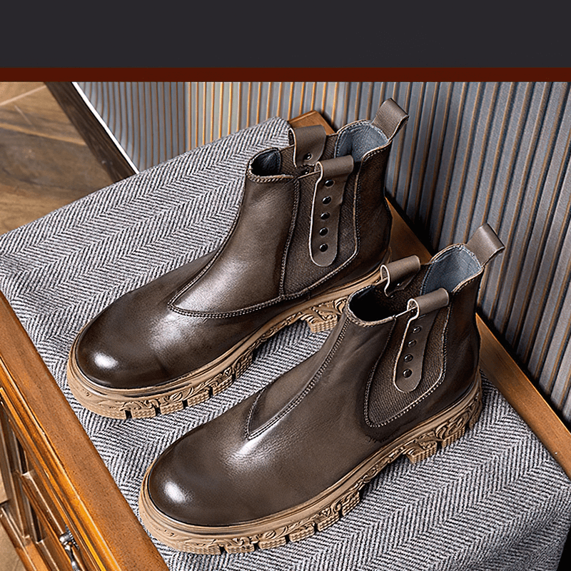 Stylish men's soft leather pull-on ankle boots with carved bottom on a textured surface.