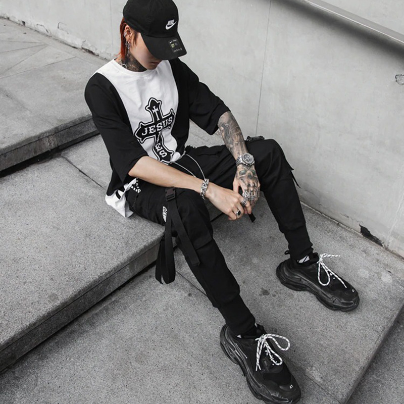 Stylish man wearing black rock style pants with ribbons, resting on steps, showcasing urban spring fashion.