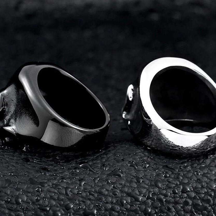 Black and silver stainless steel skull rings showing high polish and alternative fashion style on textured background.