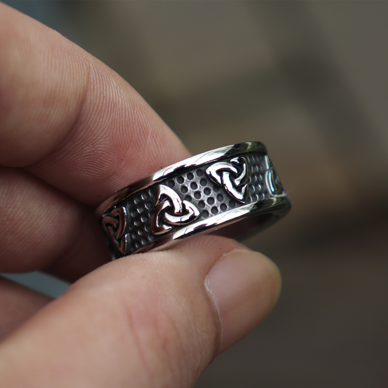 Hand holding a stainless steel Gothic style unisex ring with intricate designs and polished surface.