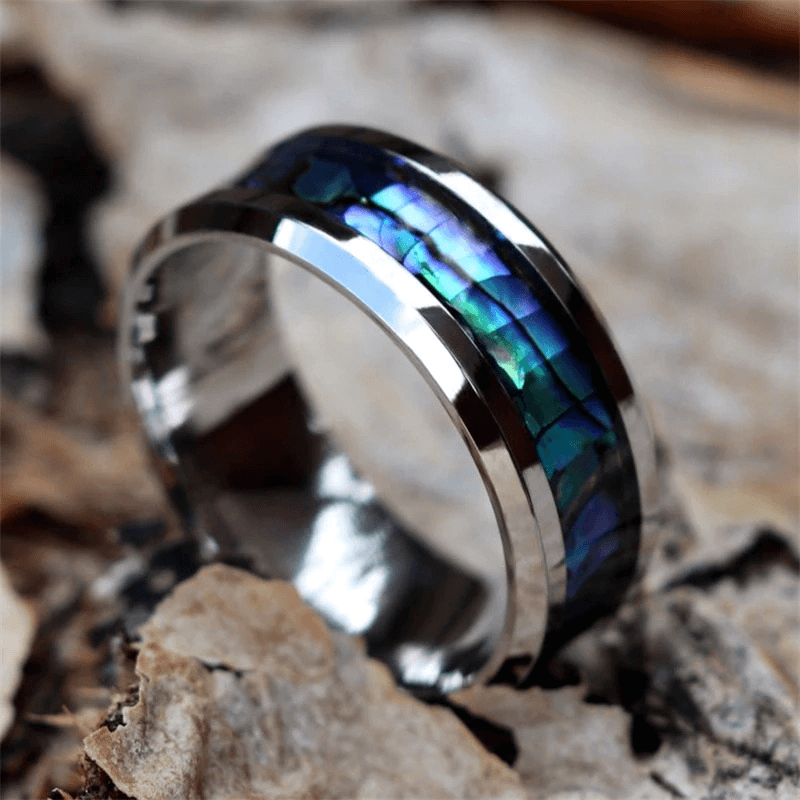 Stylish stainless steel unisex ring with vibrant abalone inlay on a rustic surface.