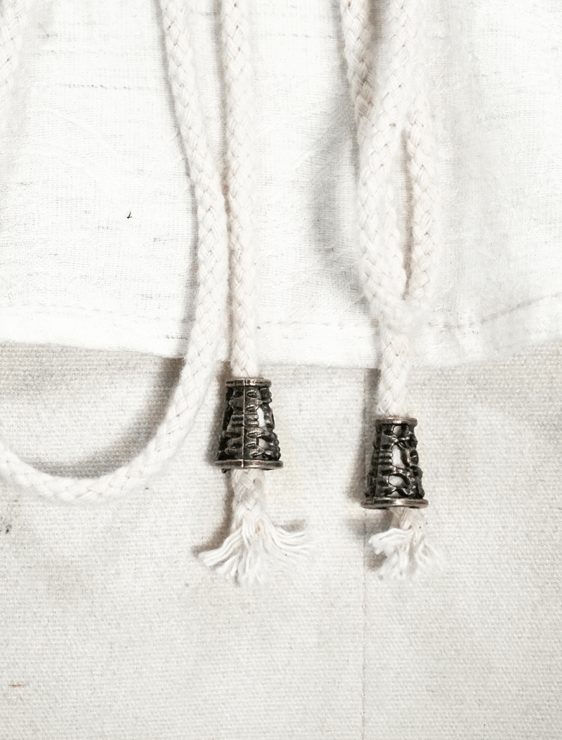 Close-up of braided drawstrings with metallic accents on a white steampunk blouse.