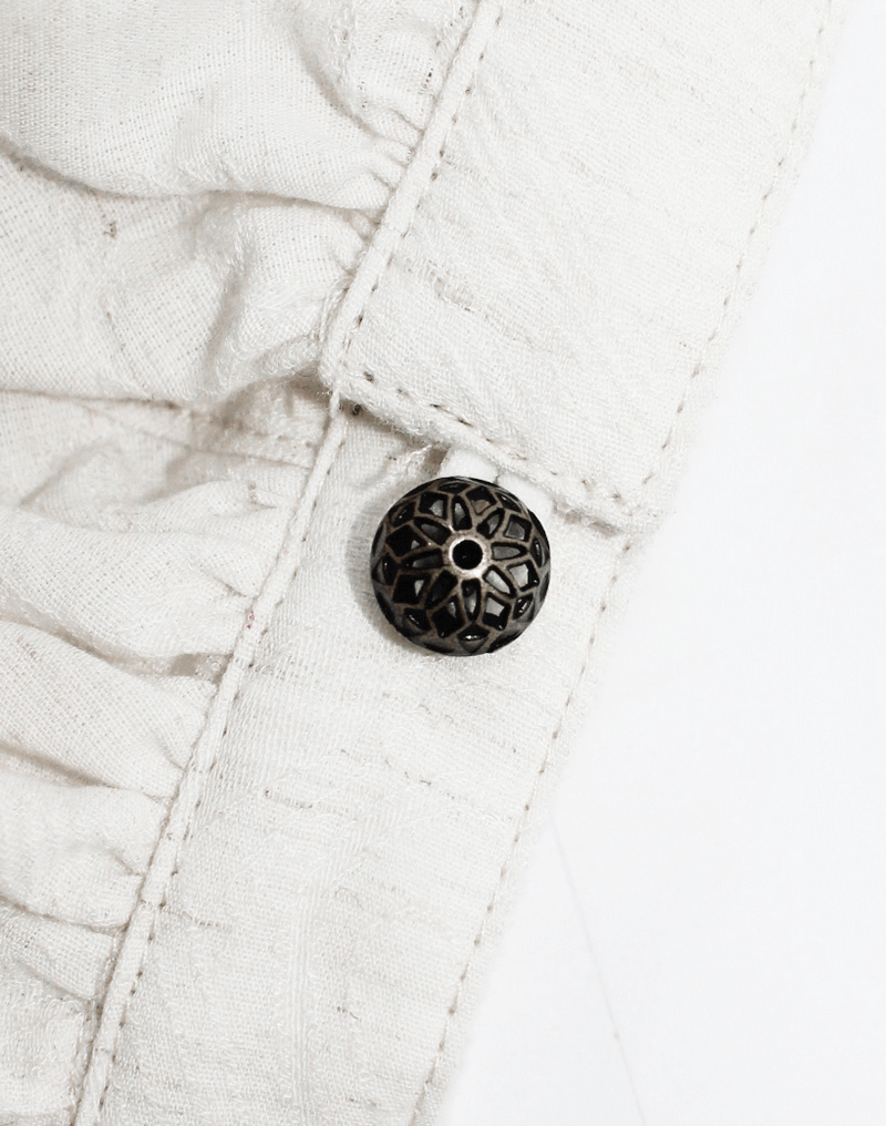Close-up of a stylish black decorative button on a steampunk women's white blouse with delicate ruffles.