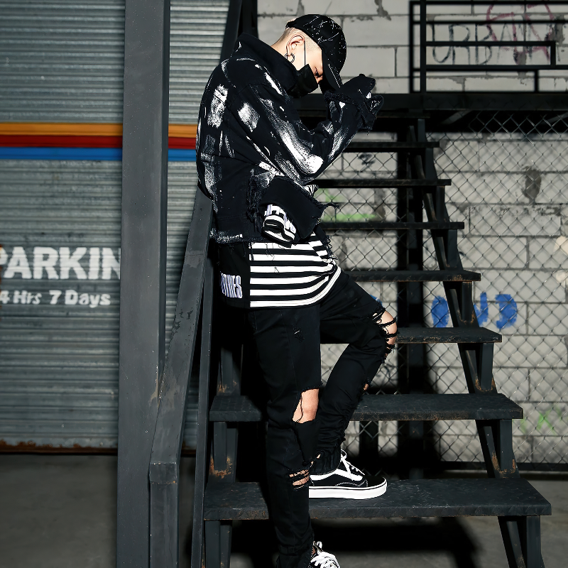 Men wearing graffiti print jeans jacket and stylish black pants on stairs, showcasing urban streetwear fashion.