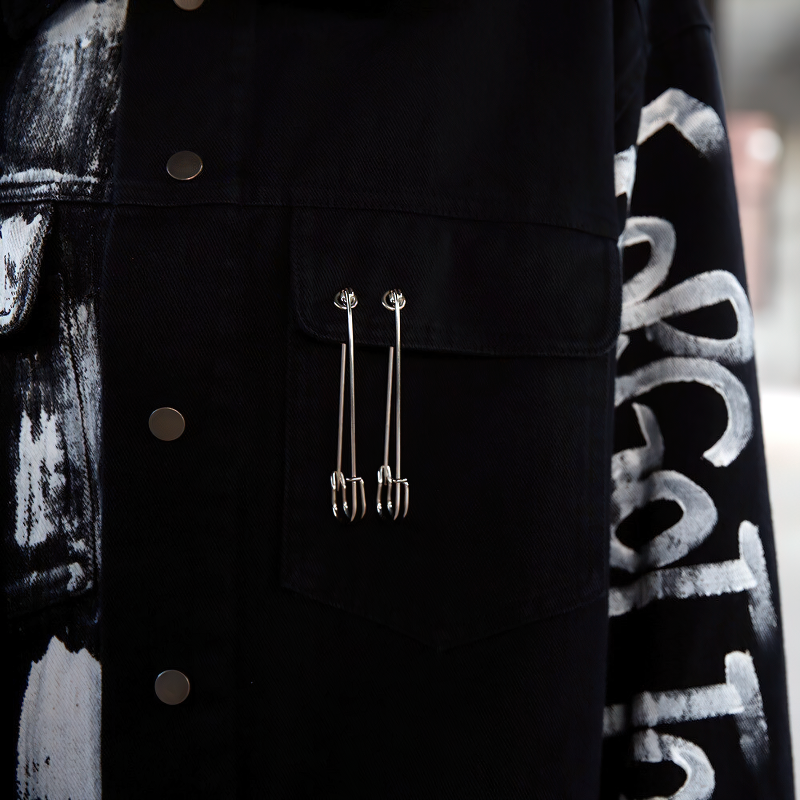 Black graffiti print jeans jacket with stylish safety pins, perfect for modern streetwear fashion.