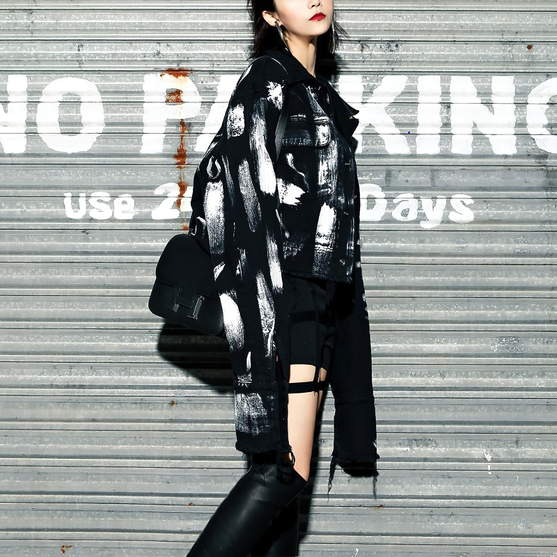 Fashionable woman wearing a black graffiti print jeans jacket, paired with edgy accessories against a street backdrop.