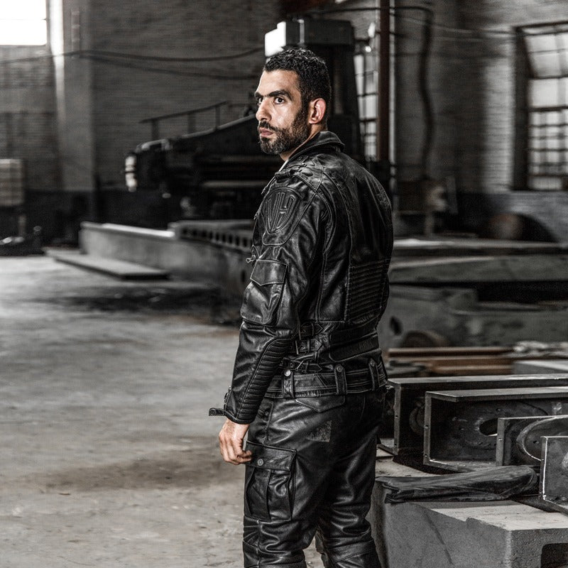 Man wearing a stylish multi-pocket genuine leather motorcycle jacket in an industrial setting.