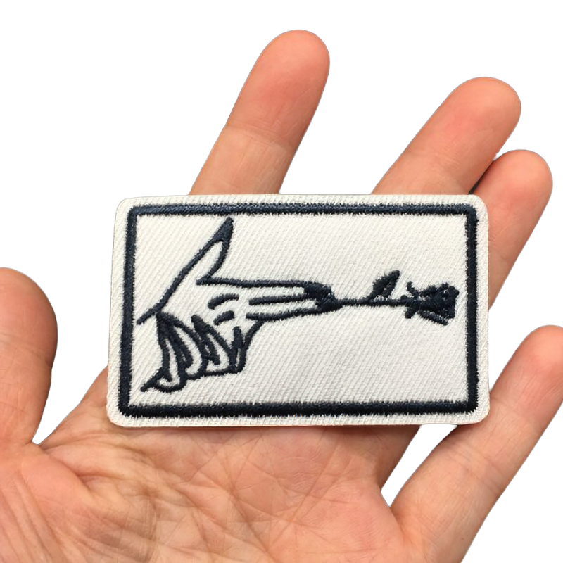 Hand holding a stylish iron-on patch featuring a finger gun and flower design, ideal for clothing decoration.