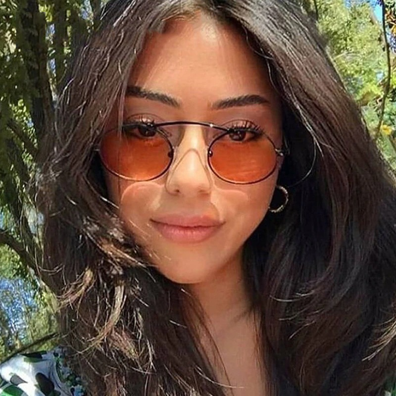 Stylish woman wearing small oval steampunk sunglasses with orange lenses, showcasing trendy summer fashion.