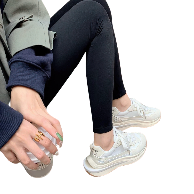 Woman wearing stylish white chunky sneakers with black leggings, holding a drink in casual outfit.
