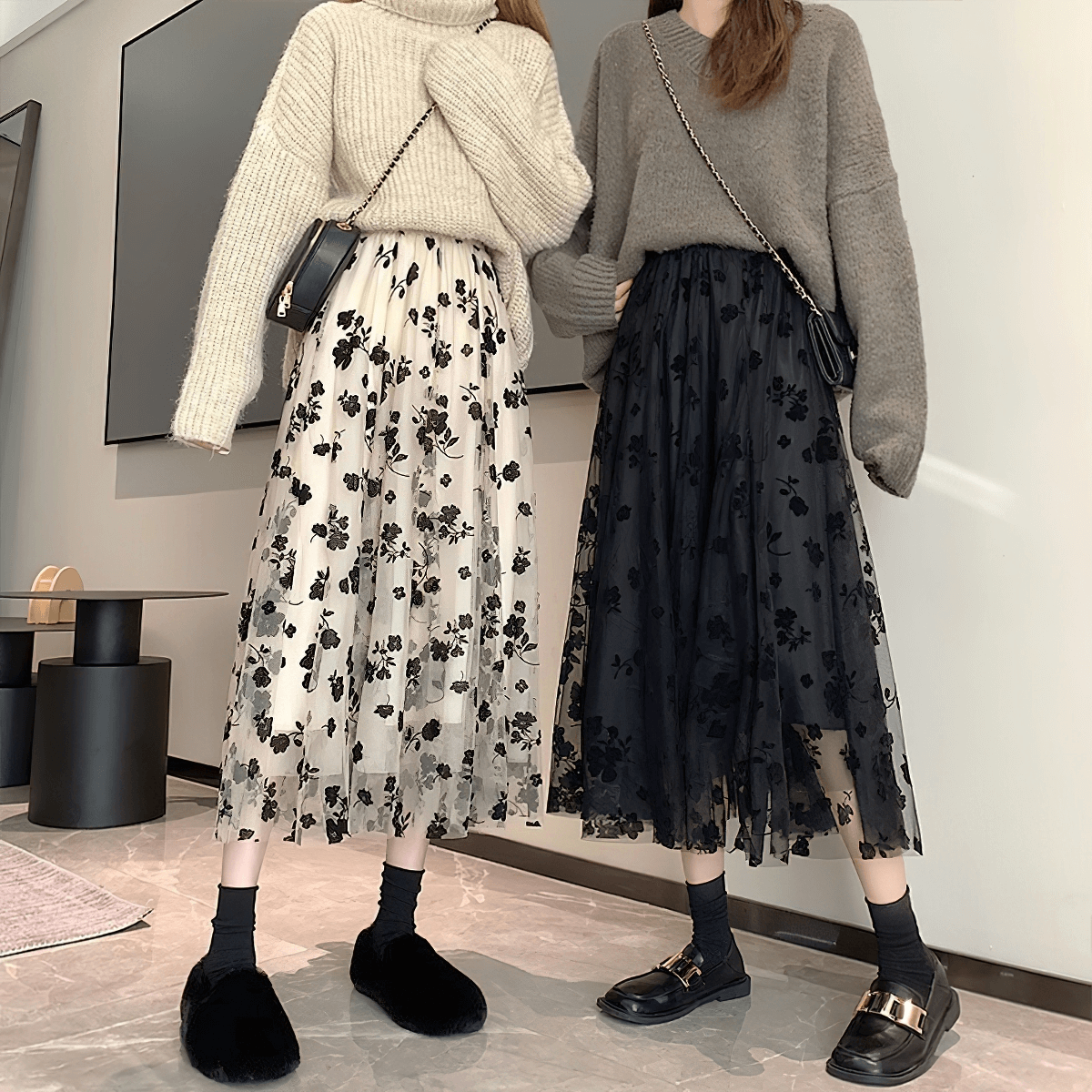 Two stylish women wearing high waist midi skirts with floral embroidery, one in black, one in cream, paired with cozy sweaters.