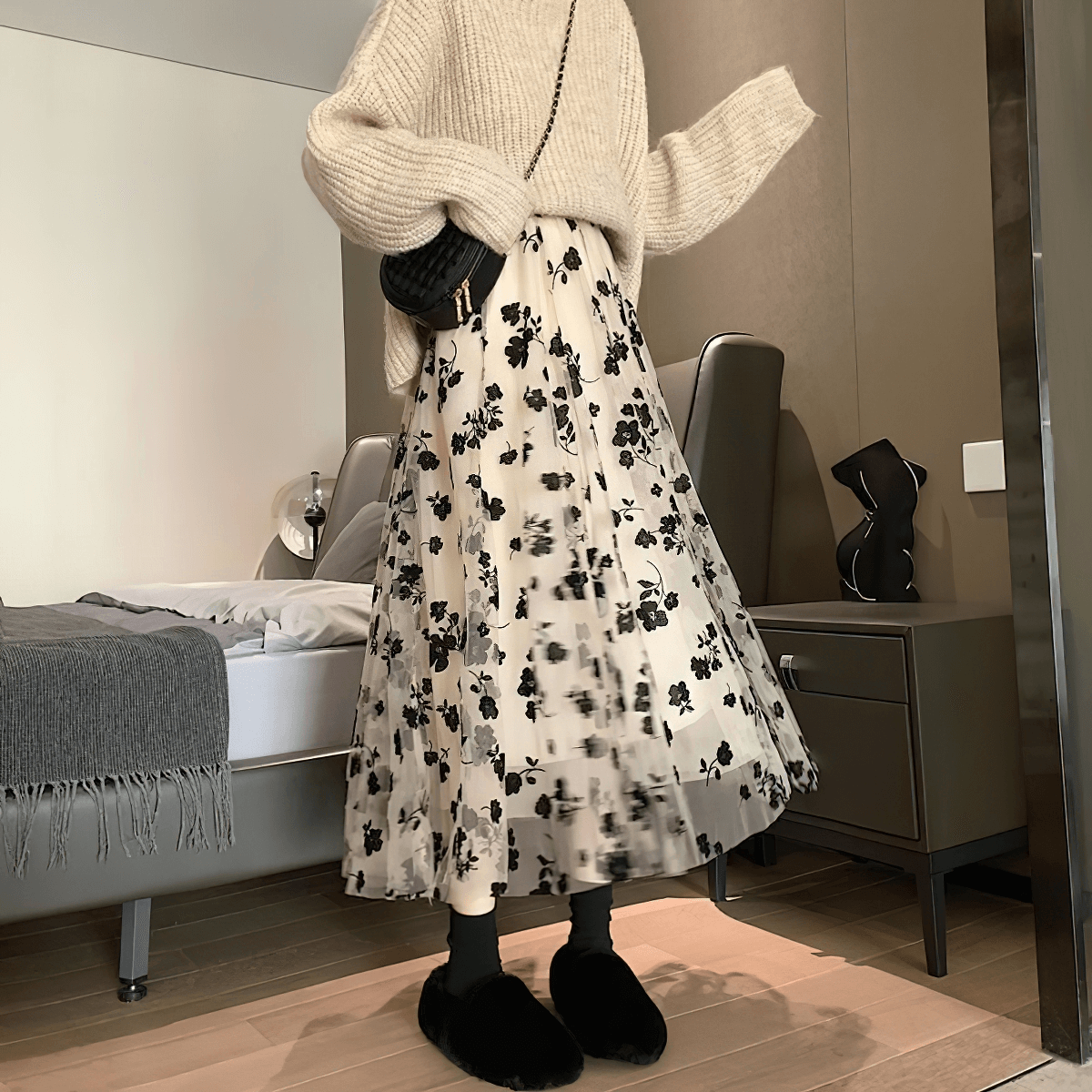 Stylish women's high waist skirt with black embroidered flowers, paired with a cozy sweater in an elegant bedroom setting.