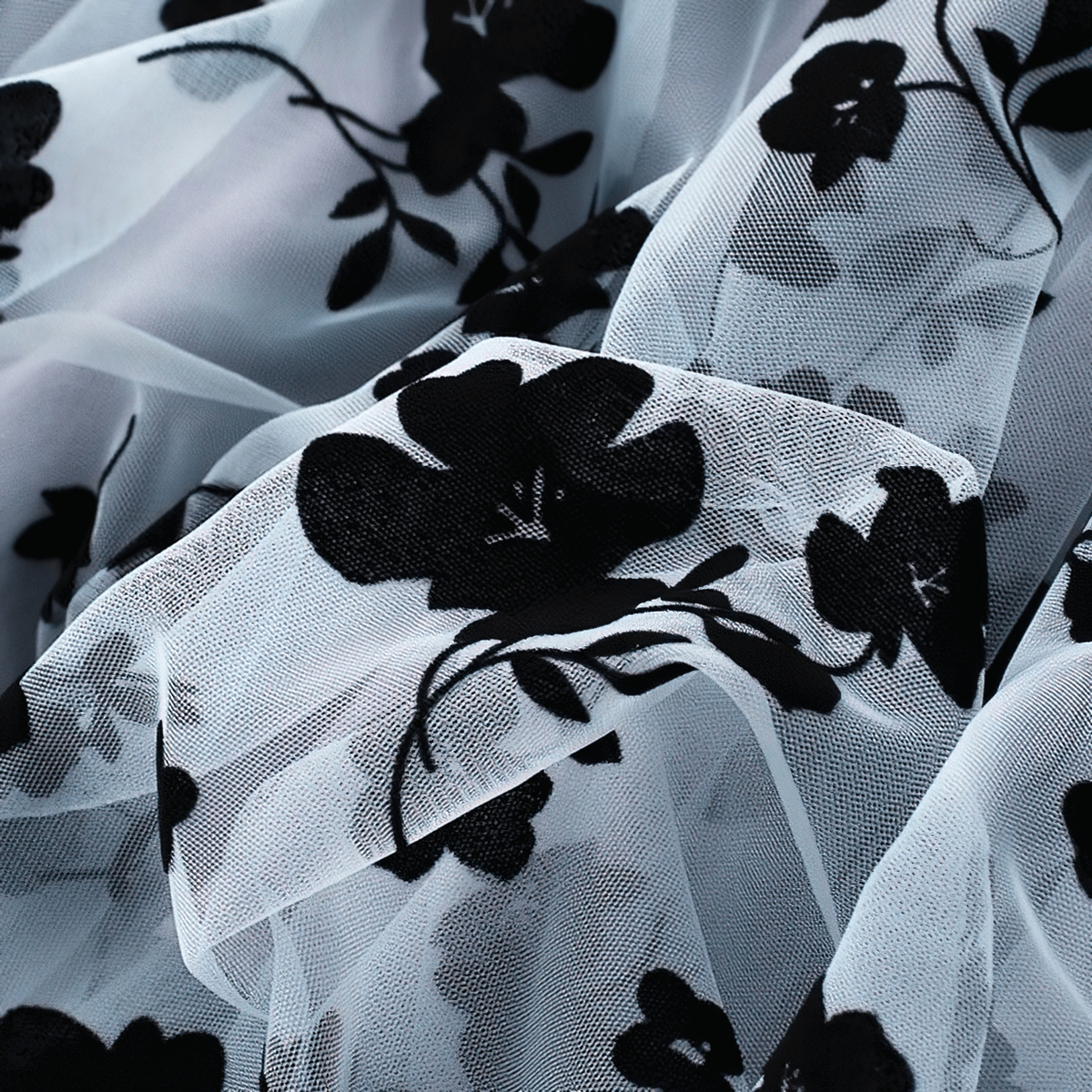 Close-up of delicate mesh tulle fabric featuring embroidered black flowers, perfect for a stylish women's skirt.
