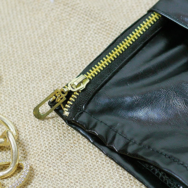 Close-up of a black faux leather pouch with a shiny gold zipper detail on a textured surface.