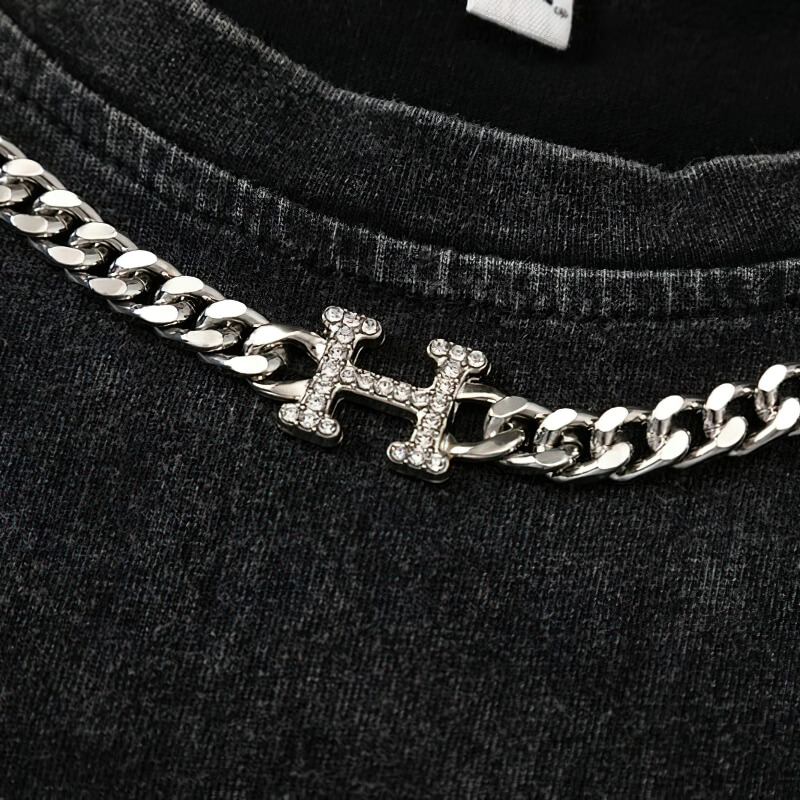 Close-up of stylish silver chain detail on a black tank top, featuring a gothic design and sparkling 'H' charm.
