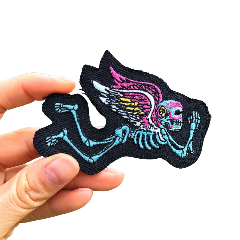 Hand holding a colorful skeleton with wings patch, perfect for customizing jackets and bags in rock style.