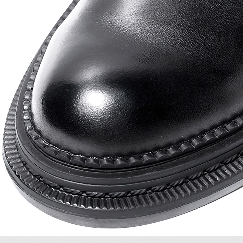 Close-up of stylish black men's ankle boot with shiny round toe and textured sole details.