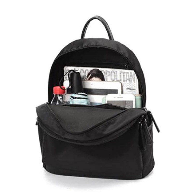 Trendy black Oxford cloth backpack for women, packed with essentials like magazines and bottles for daily use.