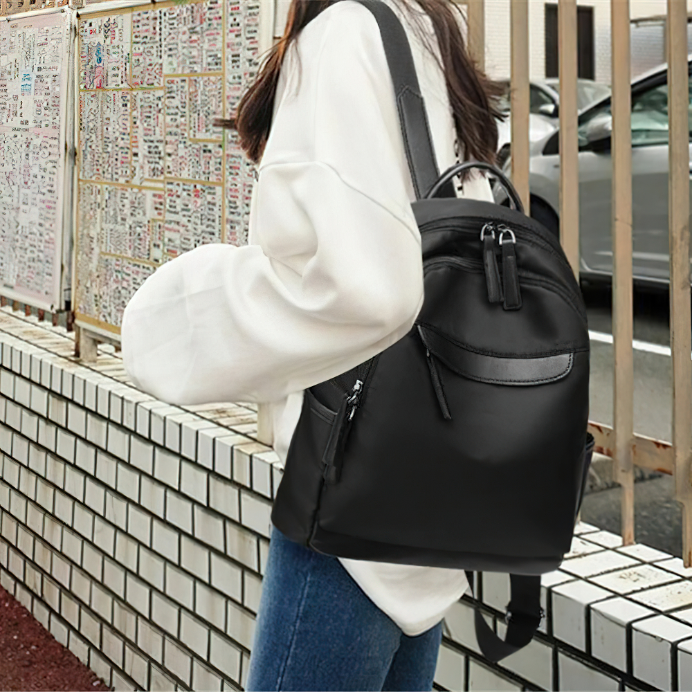 Trendy black Oxford cloth backpack casually worn by a woman, showcasing stylish design and practical pockets.