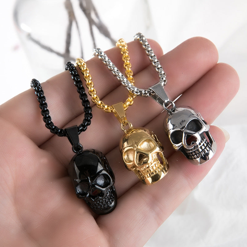 Unisex stainless steel skull necklaces in black, gold, and silver on a hand, perfect for rock style enthusiasts.
