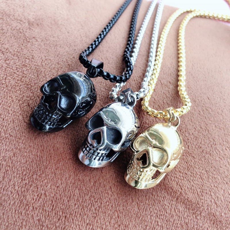 Unisex stainless steel skull necklaces in black, silver, and gold on a textured background, perfect for biker rock style.