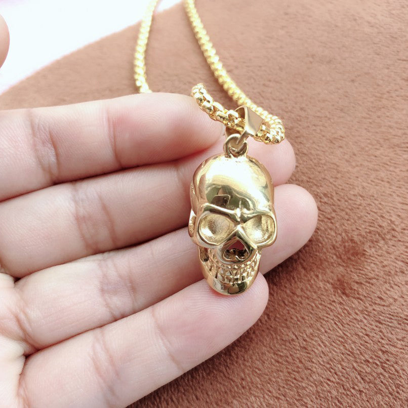 Gold stainless steel skull necklace held in hand, perfect for rock style enthusiasts and bikers.