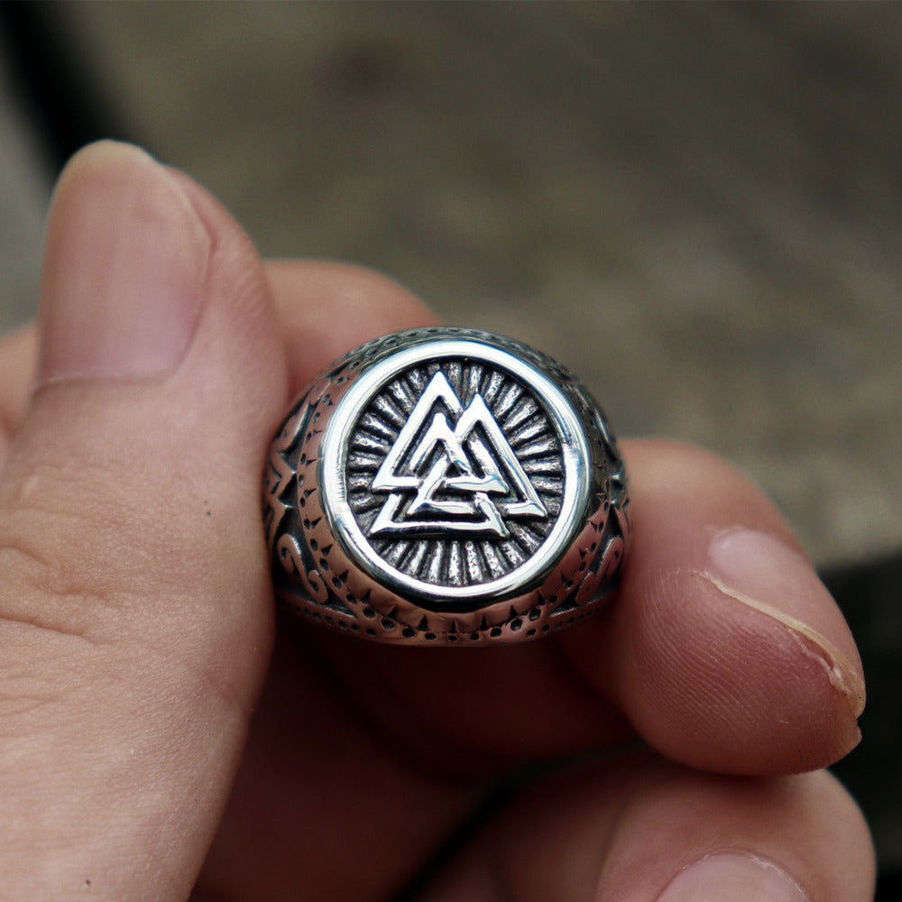 Close-up of a hand holding a Viking stainless steel ring with Valknut design, showcasing Norse runes and amulet style.
