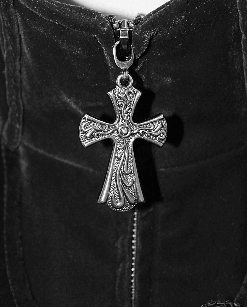 Close-up of a vintage cross zipper pull on a black velvet coat, adding gothic style to the design.