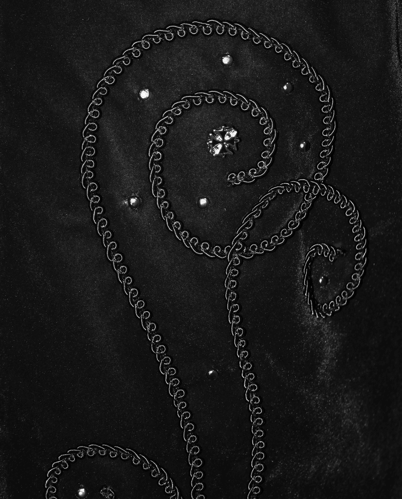 Close-up of decorative embroidery on a vintage black velvet coat, featuring elegant swirls and sparkling accents.