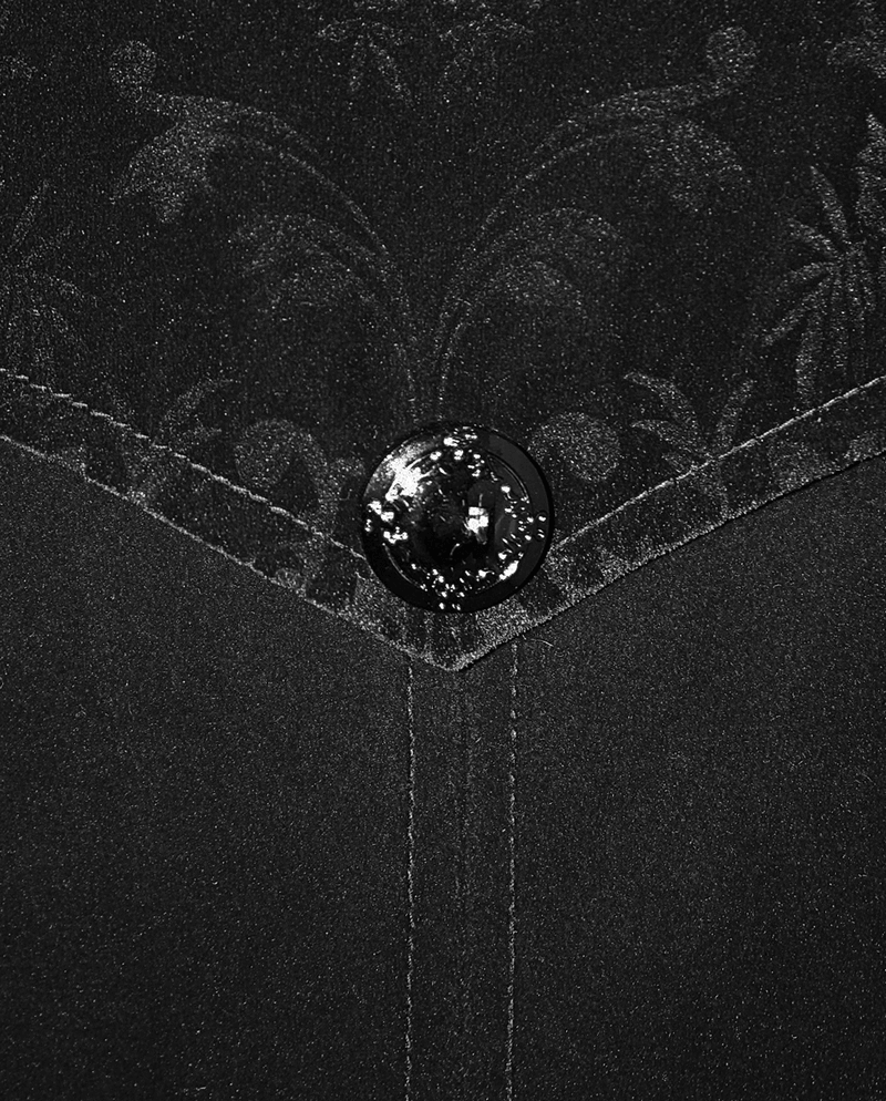 Close-up of black vintage velvet fabric with ornate pattern and stylish button detail for gothic men's coat.