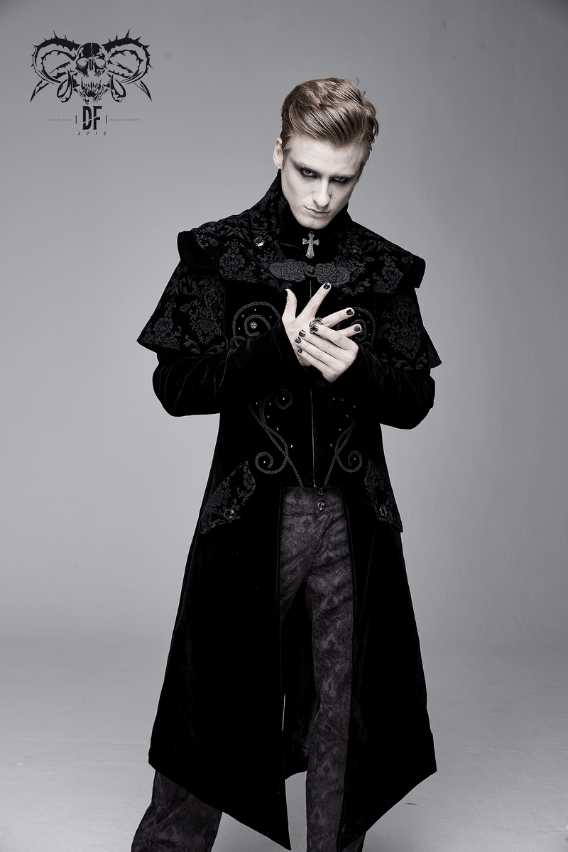 Stylish man wearing a vintage black long velvet gothic coat with cross accents, posing dramatically.