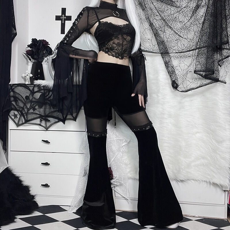 Gothic style woman wearing vintage black velvet flare pants with mesh inserts, posing against a spooky backdrop.
