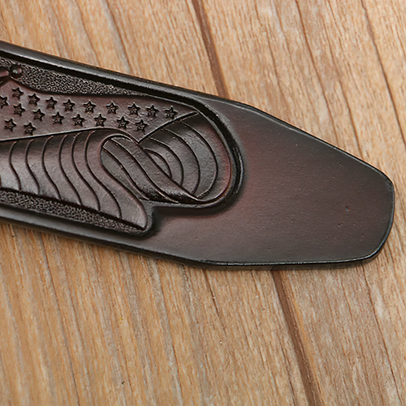 Close-up of vintage men's leather belt tip featuring eagle and stars design on wood background.