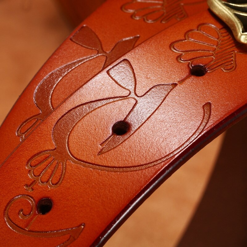 Close-up of a vintage genuine leather belt showing intricate embossed designs and pin buckle accents.