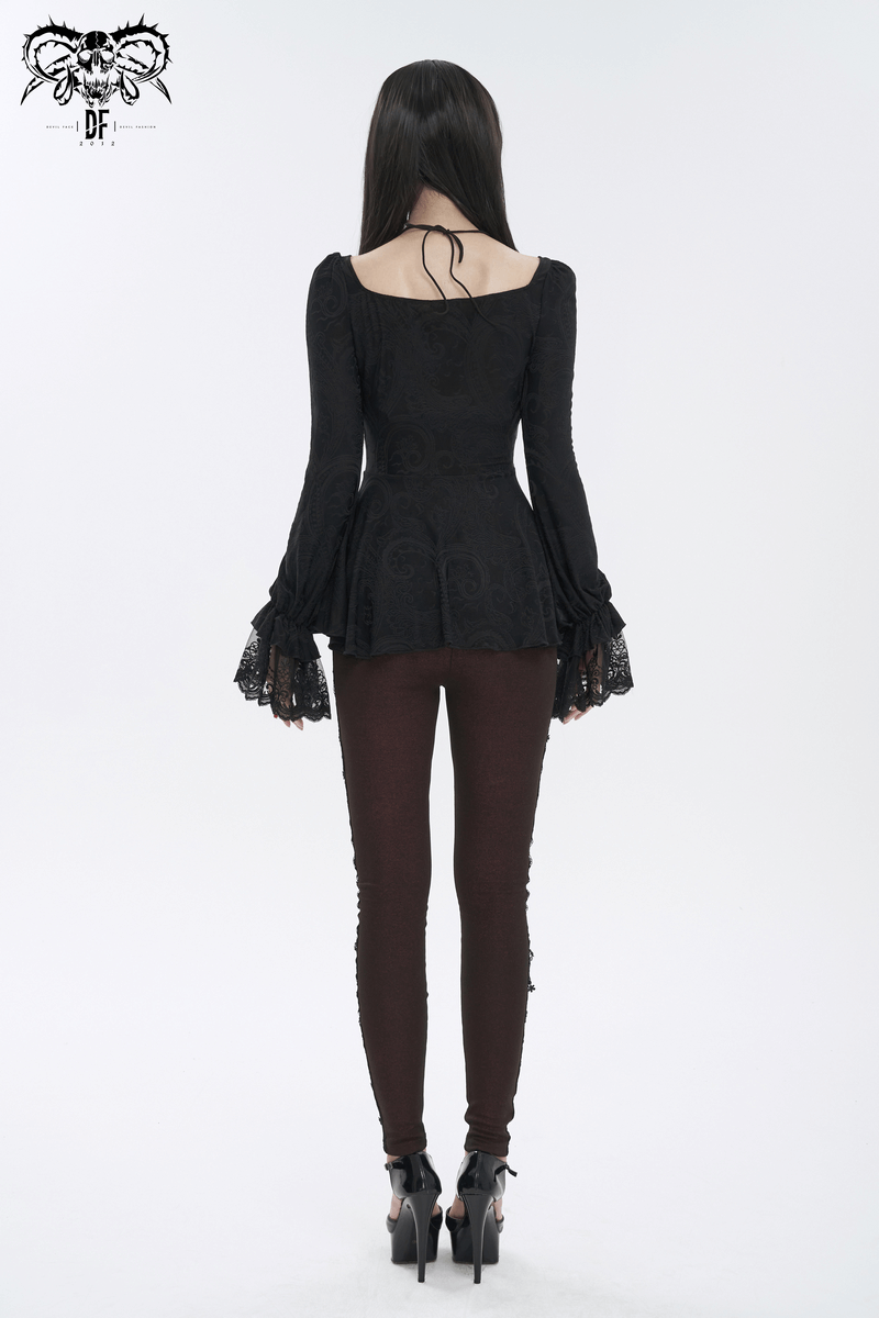 Back view of a vintage black top with flared lace sleeves and lace-up detail, paired with fitted brown pants.
