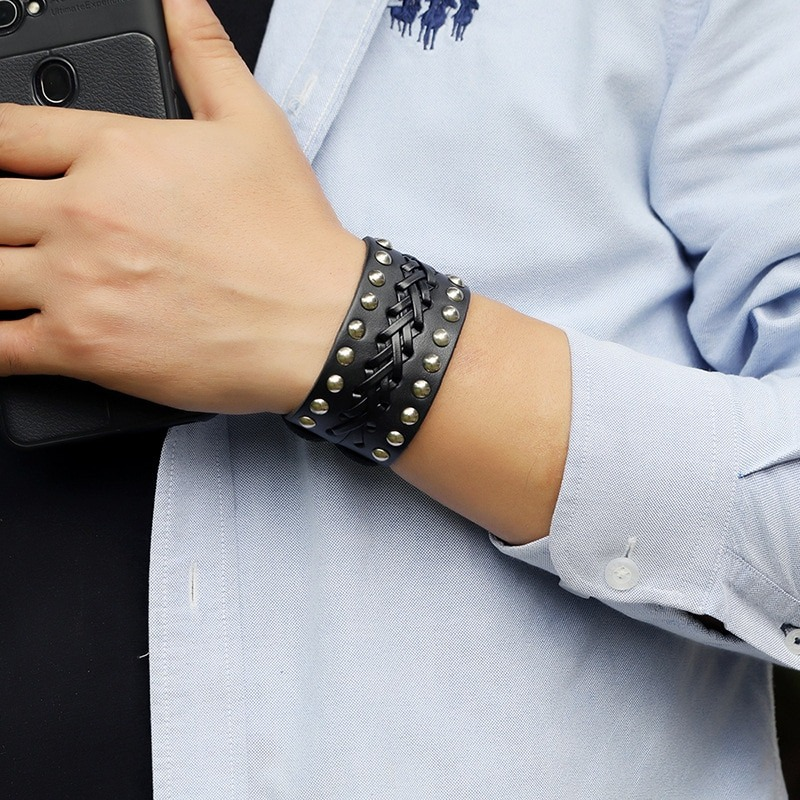Stylish punk rock wide leather bracelet with silver rivets and manual weave on a man's wrist.