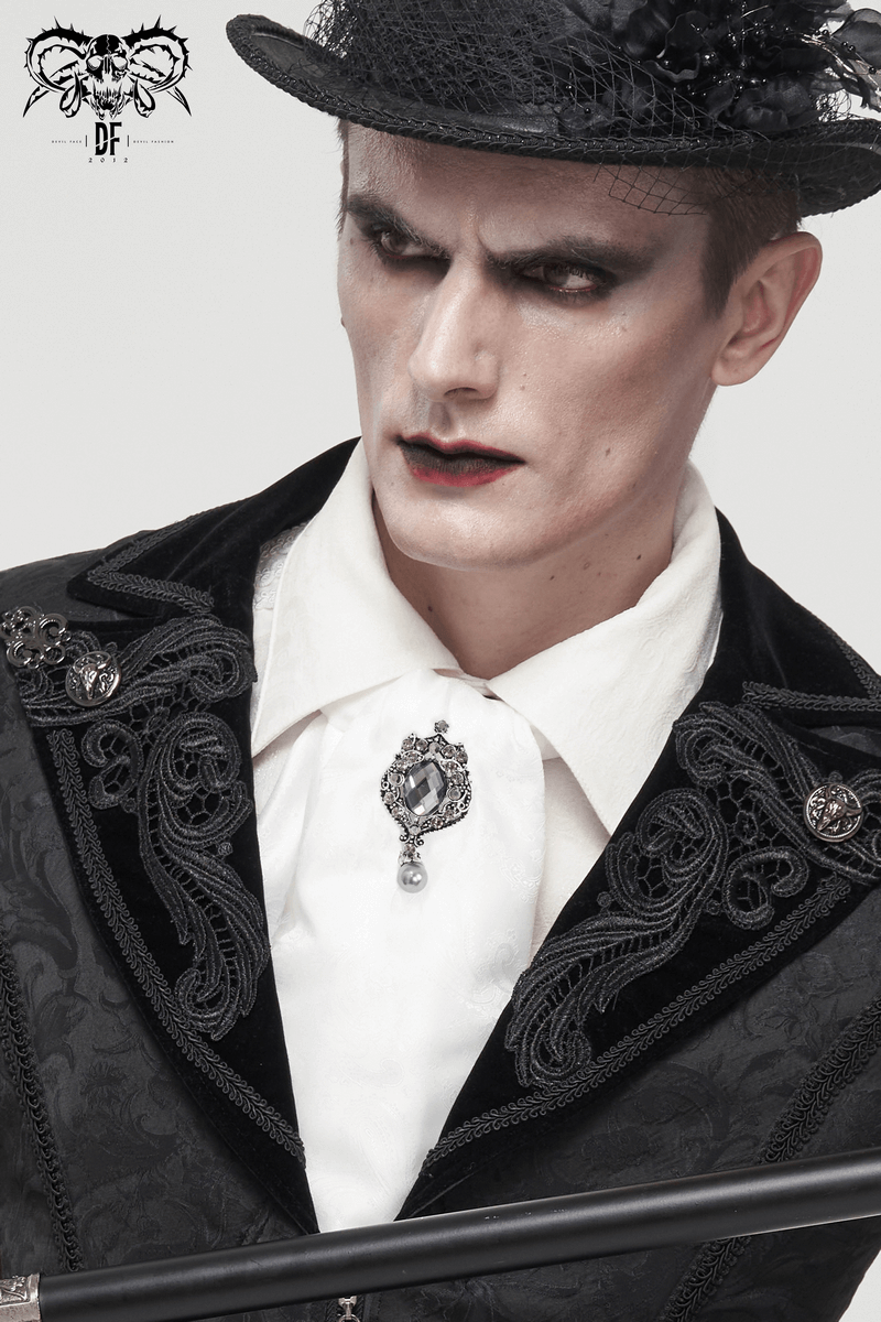 Close-up of a gothic man in a black velvet coat, white shirt, and a crystal brooch, showcasing vintage style and dramatic makeup.